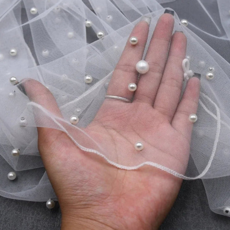 Ivory tulle shawl edge with pearl beads and dangling strand held in hand