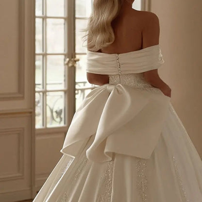 Off-shoulder satin bridal gown with draped bow and beaded waist detailing