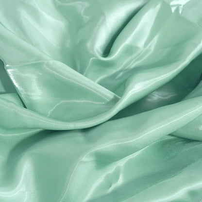 Light mint glossy satin fabric close-up with flowing folds and bright sheen