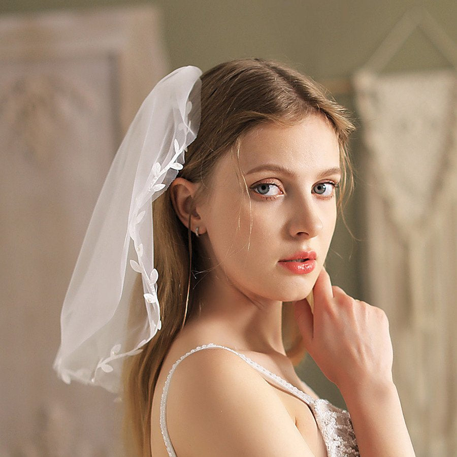 Ivory short veil with lace trim and leaf appliqué, tucked near updo