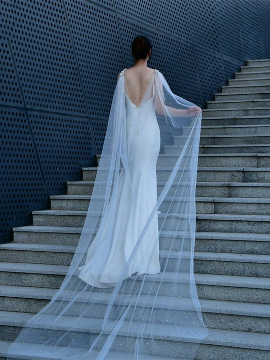 White tulle bridal cape veil drapes over back with crystal and pearl neckline trim